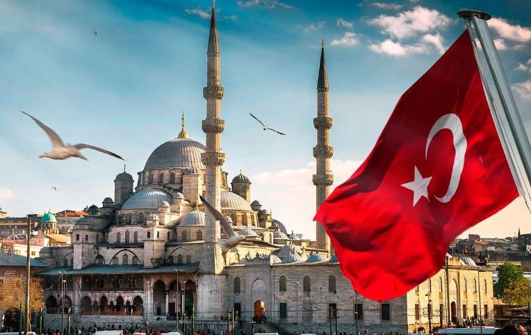 عکس مسجد ایاصوفیه در استانبول که سمت راست آن پرچم ترکیه است و پرنده ها اطراف آن در حال پرواز اند - هزینه سفر به ترکیه
